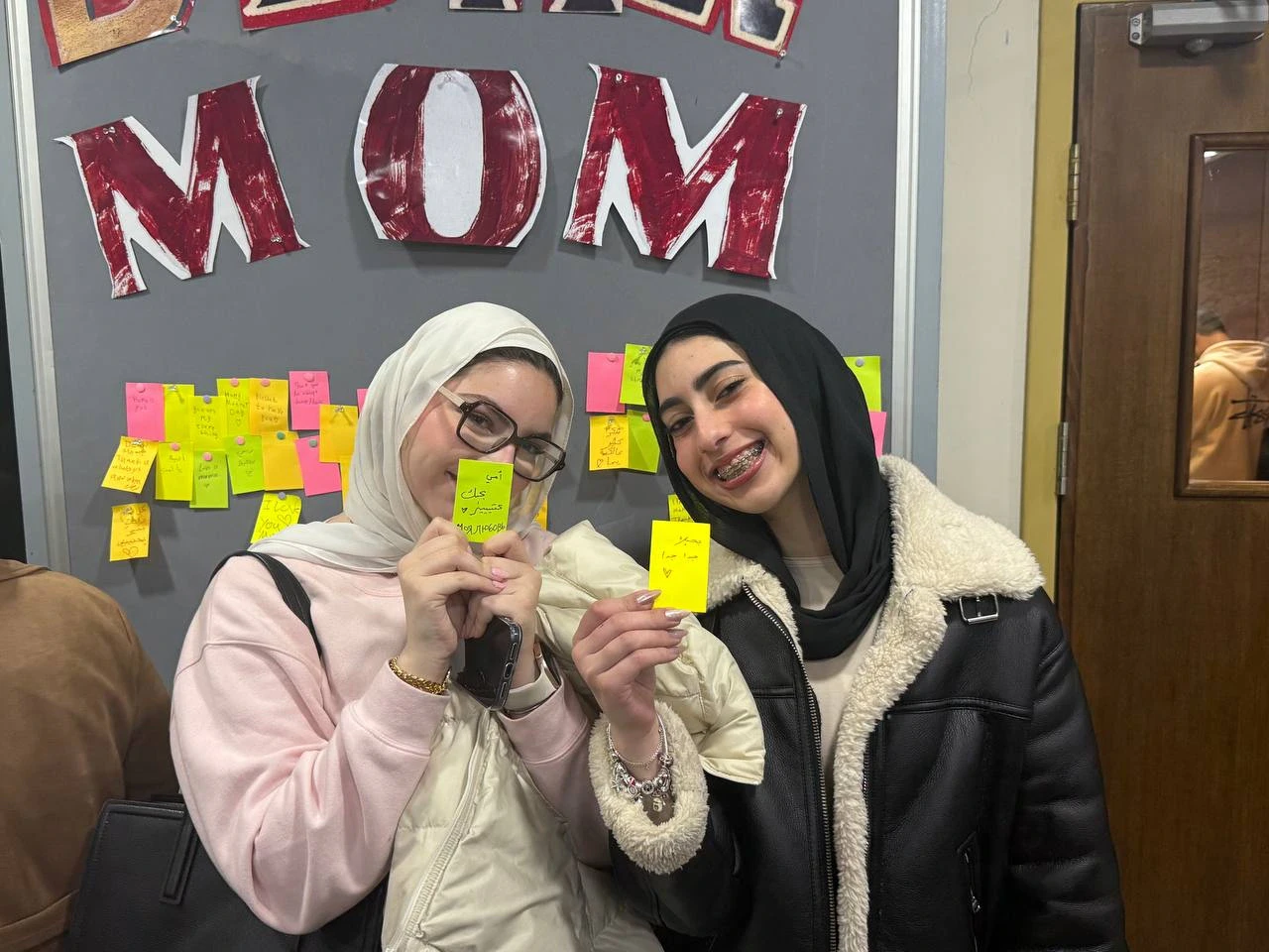 Two people holding colorful handwritten notes beside a display